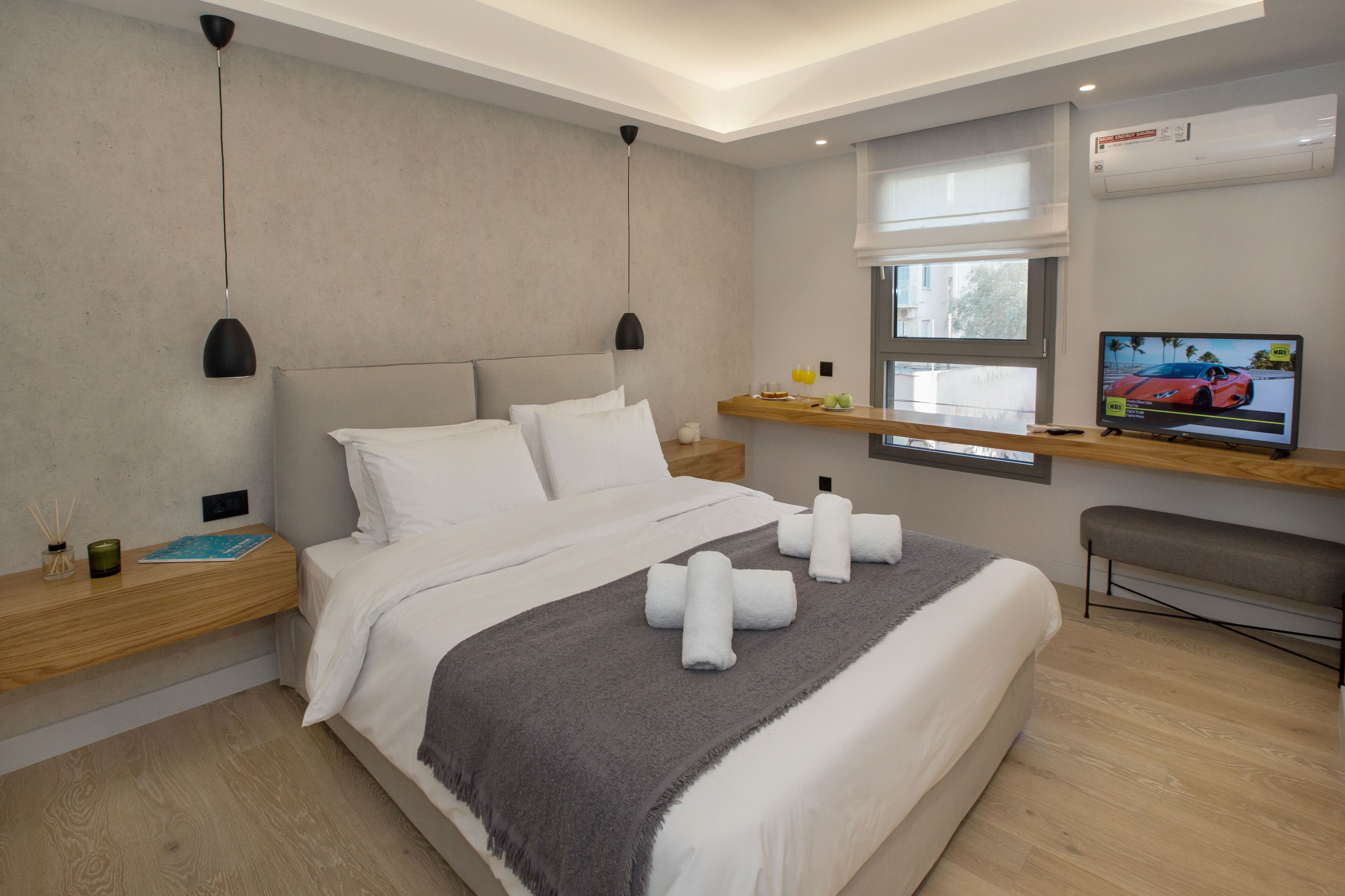 A modern hotel room with a large bed, a TV, a window, and a wooden nightstand.