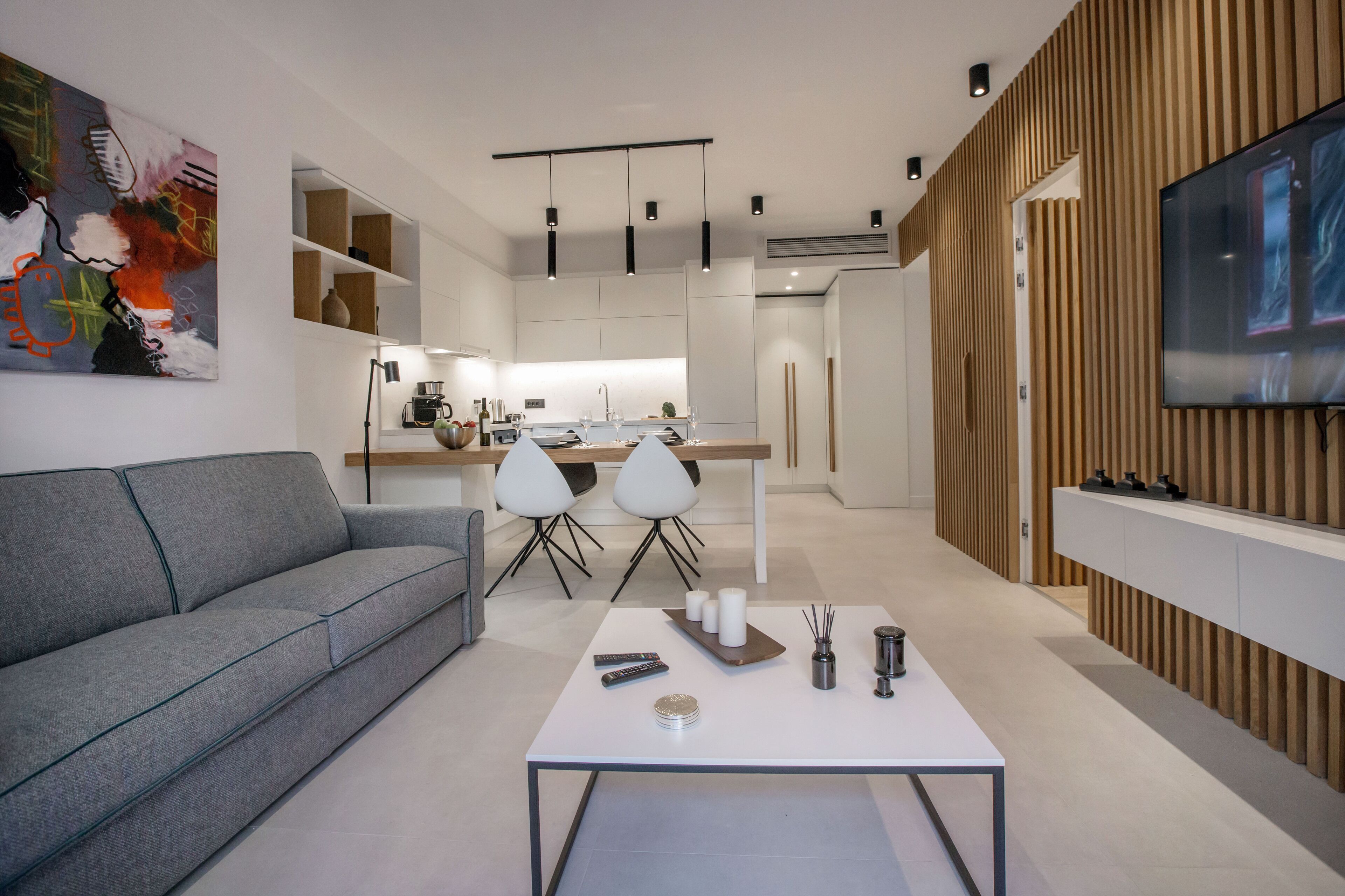 Un soggiorno moderno con un divano grigio, un tavolino da caffè bianco e una TV a parete.