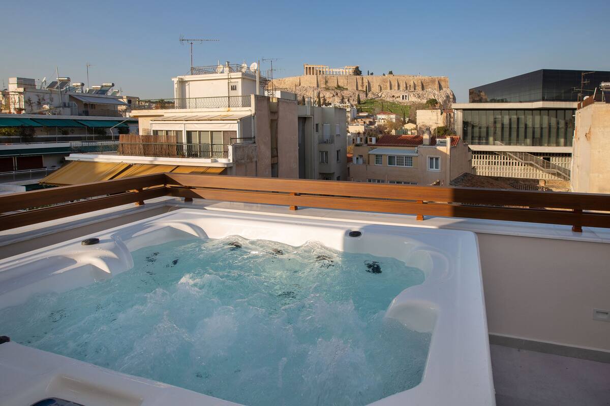 A rooftop hot tub with a wooden deck, overlooking a cityscape with historic buildings and a fort.