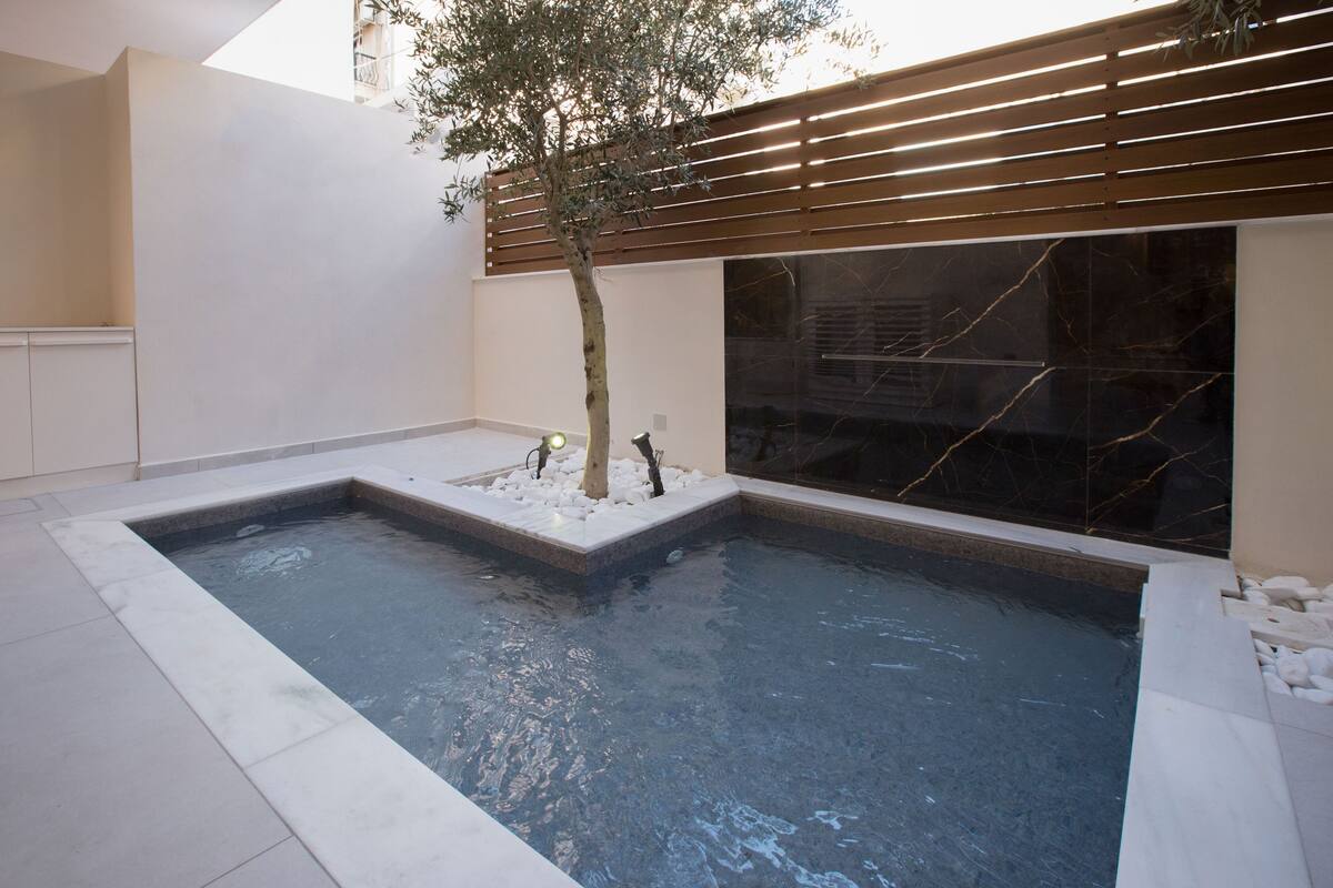 A modern indoor pool with a tree and a wooden slatted wall.