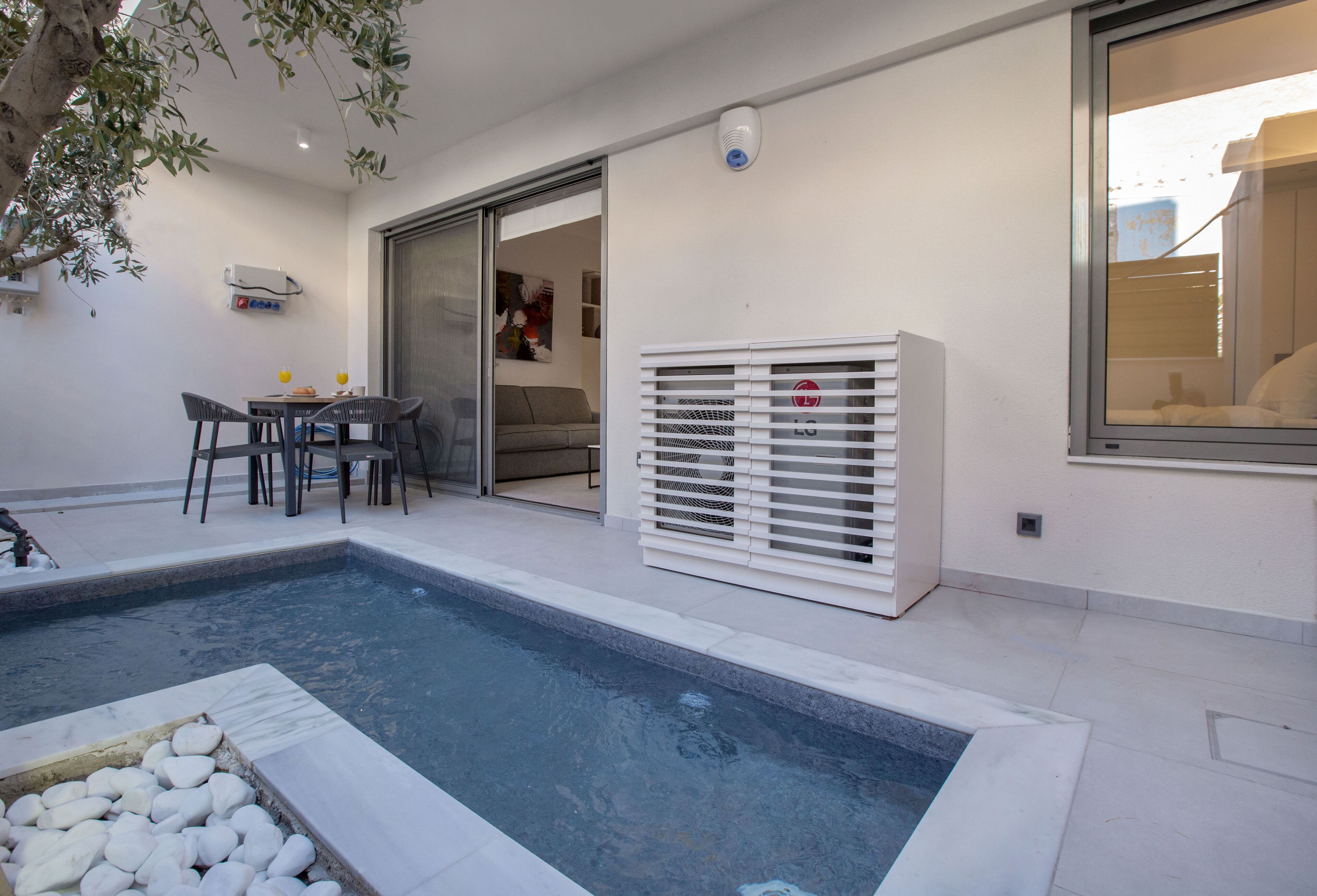 A modern outdoor pool area with a seating area, a water feature, and a sliding glass door leading to an interior space.
