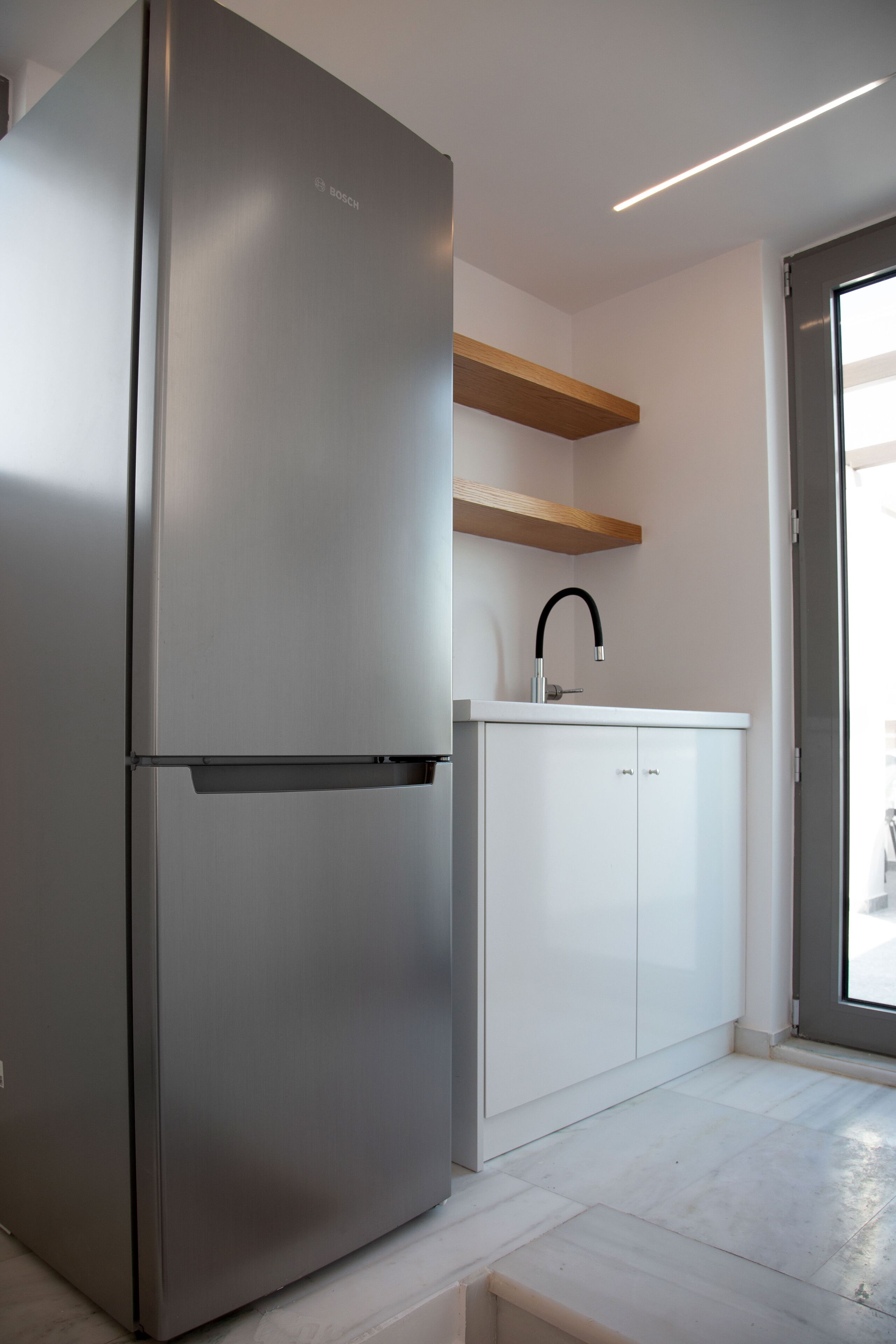 A modern kitchen with a stainless steel refrigerator, white cabinets, and a wooden shelf.