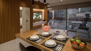 A modern dining area with a wooden table set for four, a television mounted on a wooden wall, and a view of the city through large windows. - Acropolis Golden Suites by GHH (Athens)