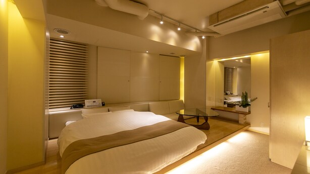 Une chambre moderne avec un grand lit, des tables de chevet, un petit coin salon et un miroir.