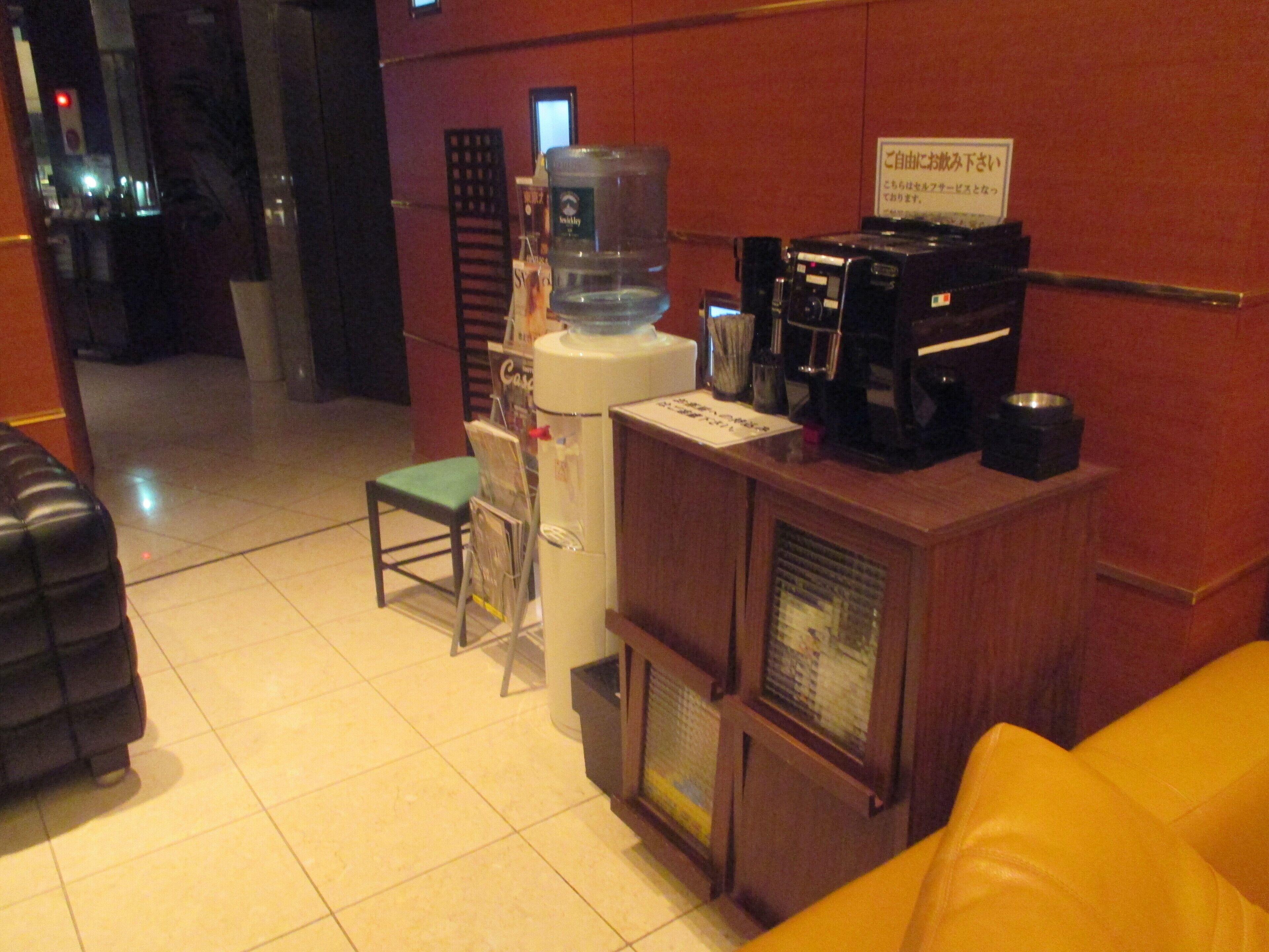 A small, compact room with a wooden cabinet, a water dispenser, a coffee machine, and a chair.