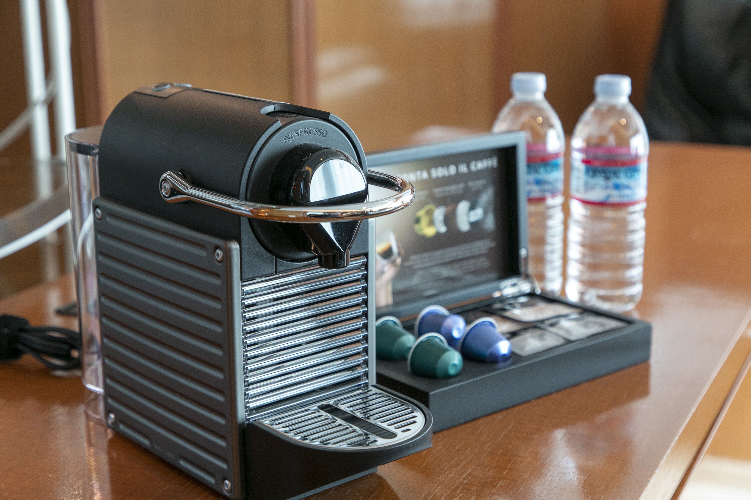 A coffee machine with a digital display, water bottles, and coffee pods on a table.