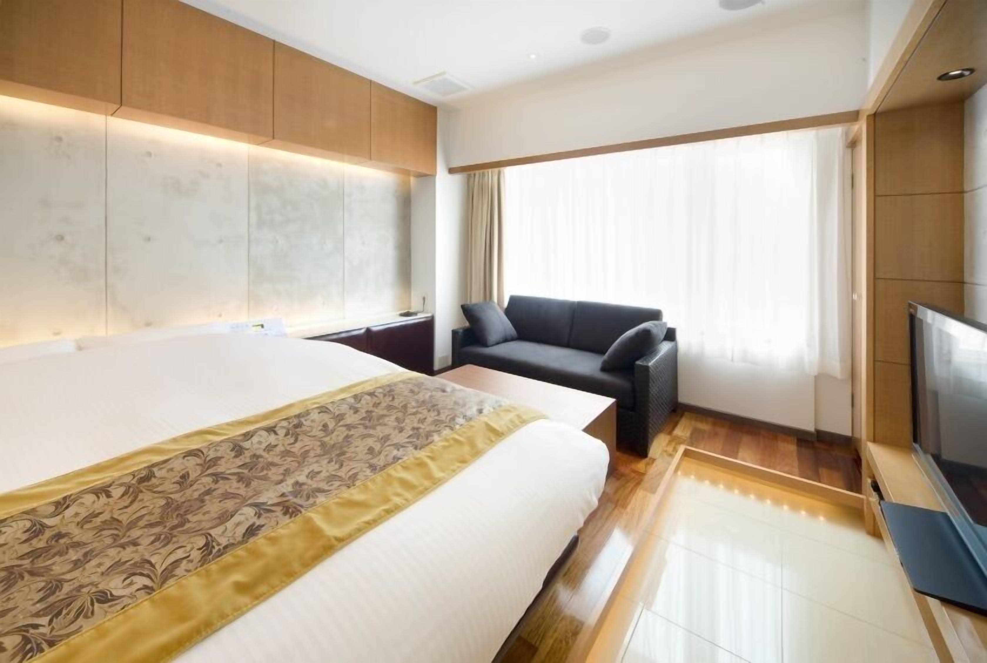 A hotel room with a large bed, a sofa, a TV, and a window with curtains.