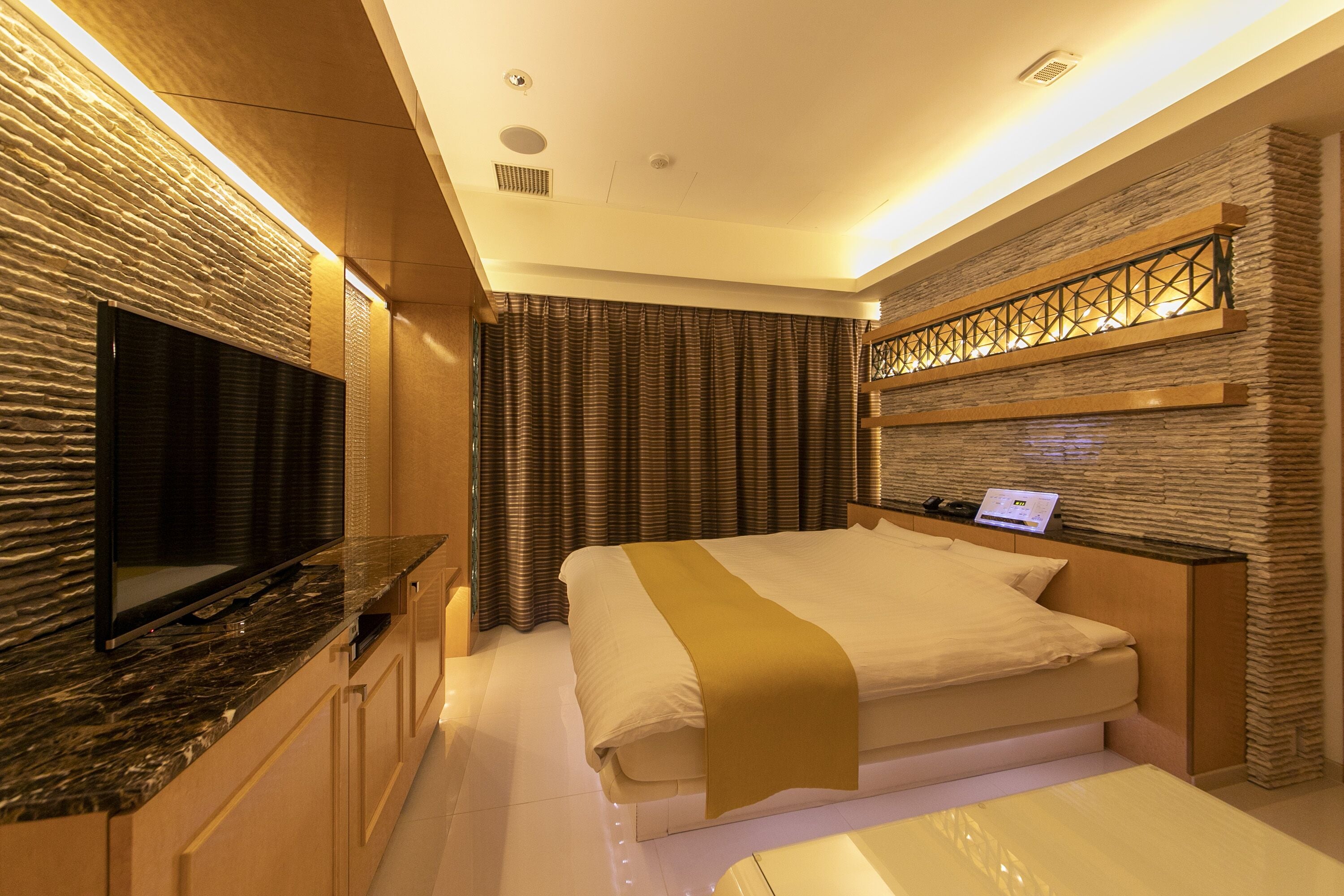 Quarto de hotel moderno com uma cama grande, uma TV de tela plana e uma escrivaninha com um laptop.