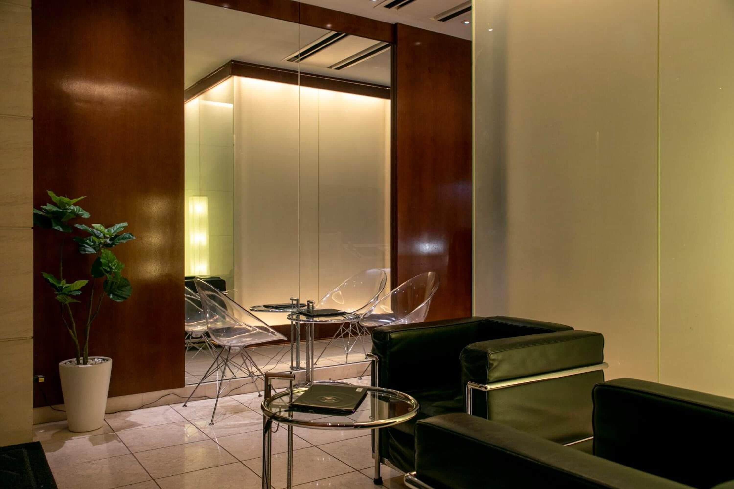 A modern lobby with a green sofa, clear chairs, a small table, and a potted plant.