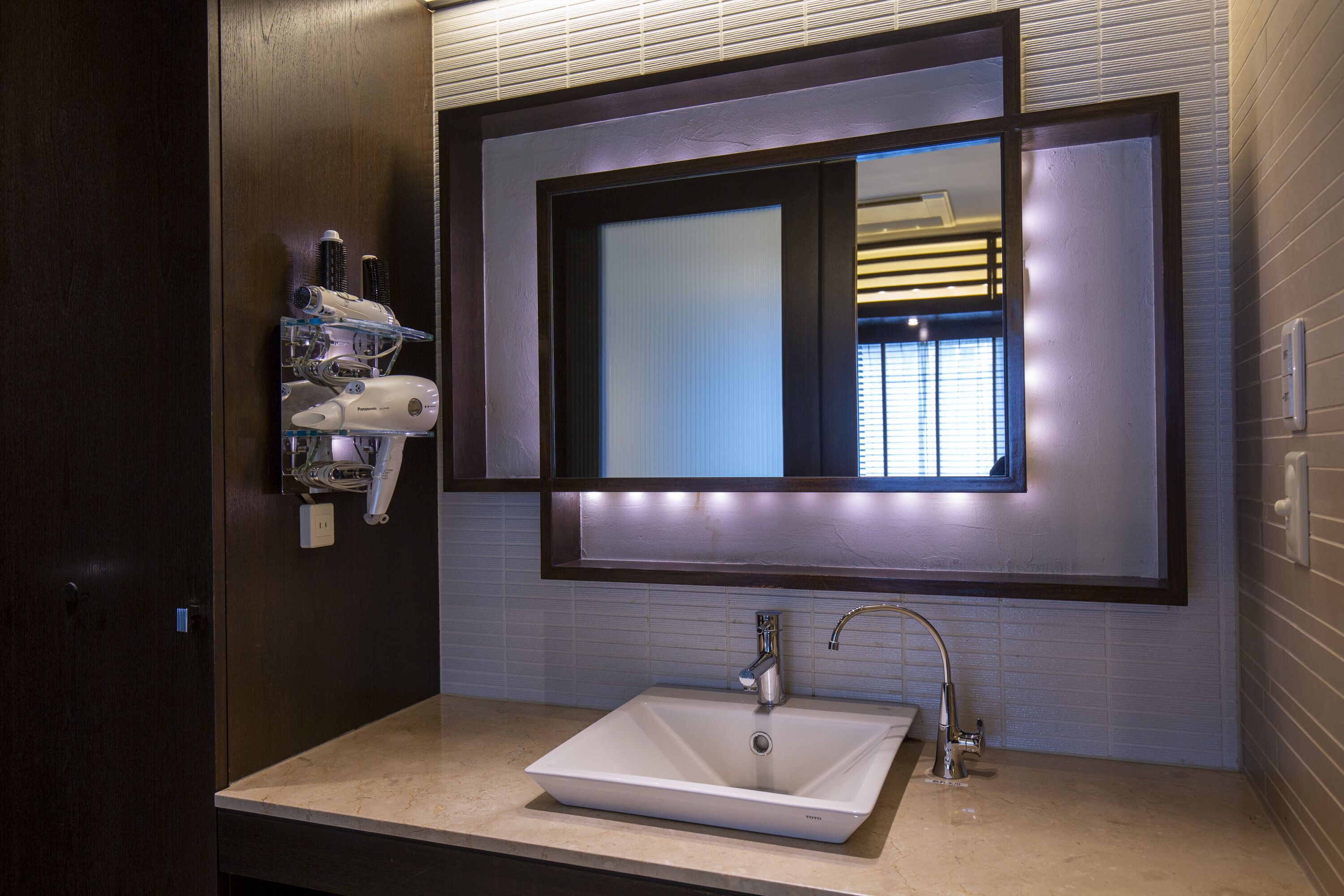 A modern bathroom with a large mirror, a white sink, and a hairdryer mounted on the wall.