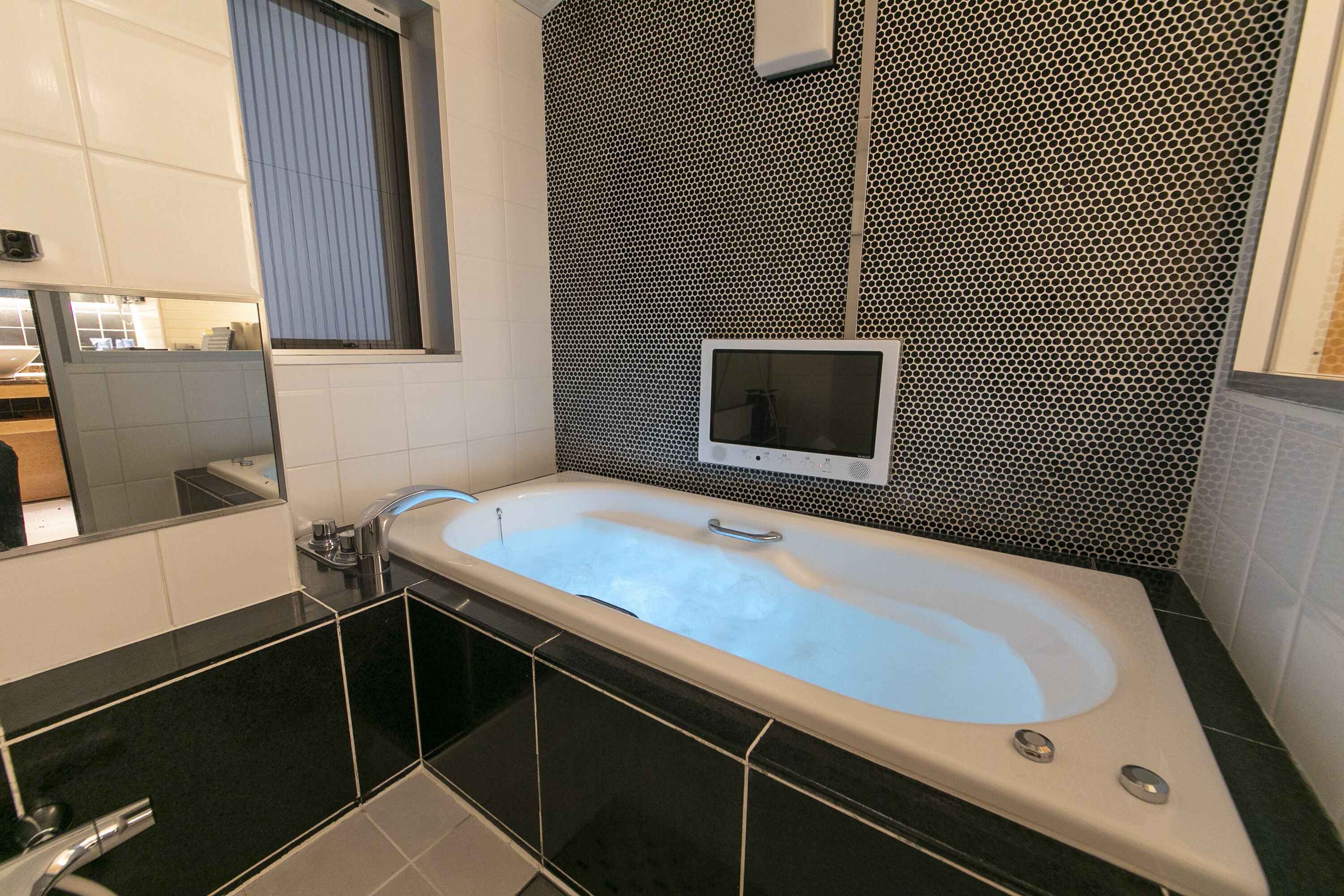 A modern bathroom with a freestanding bathtub, a large mirror, and a black and white patterned wall.