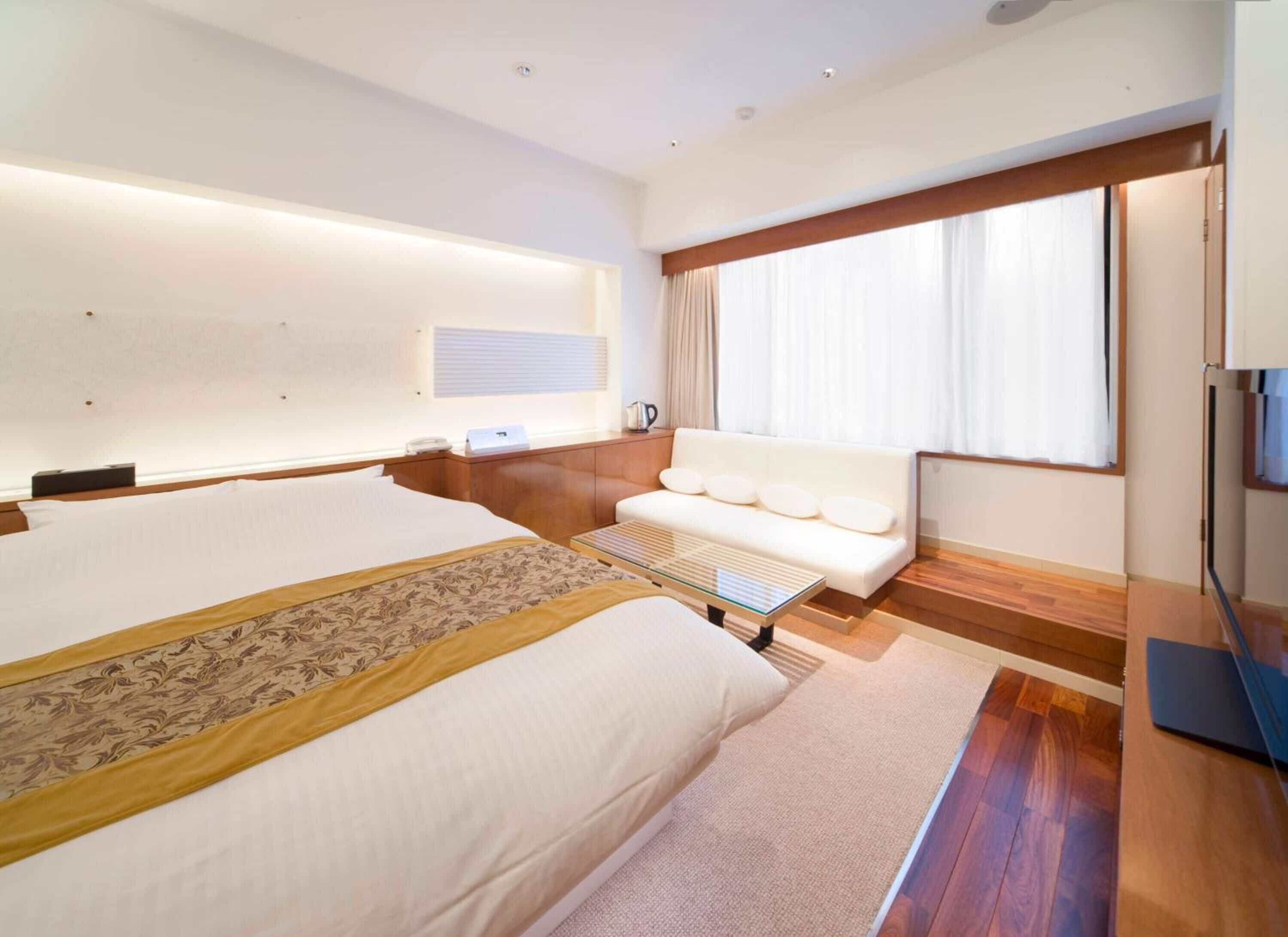 A hotel room with a large bed, a sofa, a desk, and a window with curtains.