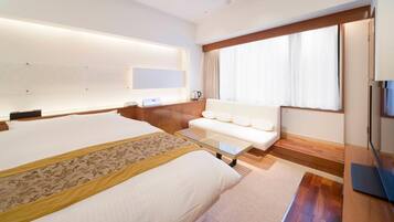A hotel room with a large bed, a sofa, a desk, and a window with curtains.