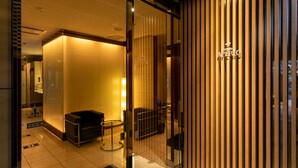 L’entrée de l’hôtel comprend un comptoir d’accueil, un espace d’attente avec un canapé et un mur en bois sur lequel est inscrit le nom de l’hôtel.