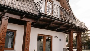 A modern house with a balcony, a stone foundation, and a wooden door.