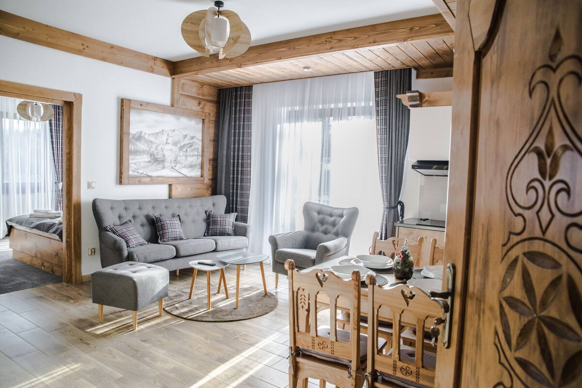 A cozy living room with a grey sofa, a wooden dining table, and a grey armchair.