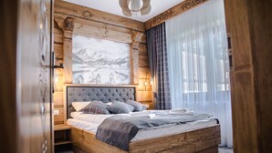 A wooden-framed bedroom with a large bed, a mounted painting, and a window with sheer curtains.