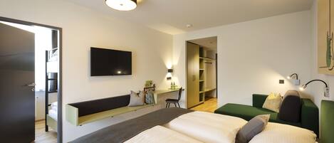 Une chambre d’hôtel moderne équipée d’un lit, d’un bureau, d’un canapé vert et d’un téléviseur fixé au mur.