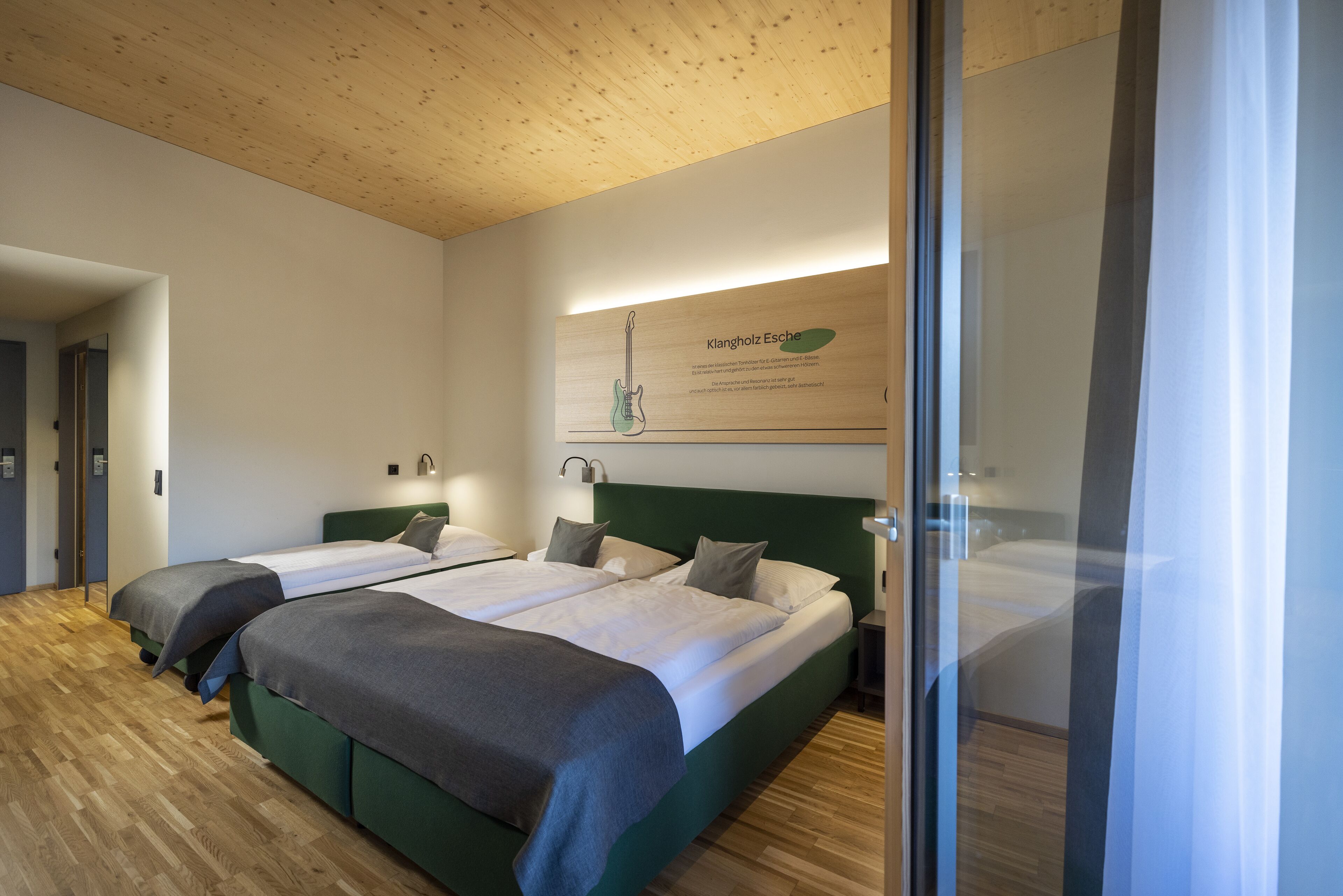 Habitación de hotel con dos camas, suelo de madera, cabecera verde y cartel en la pared.