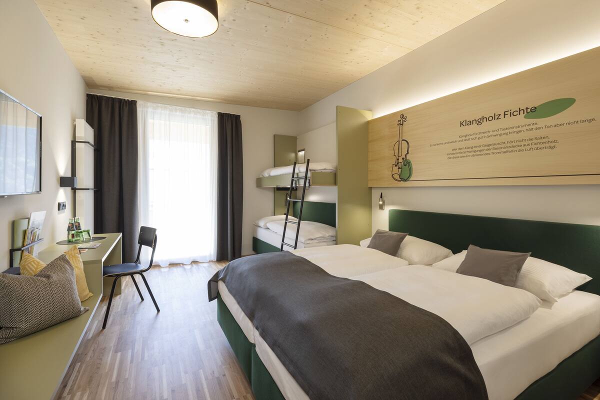 Een hotelkamer met een stapelbed, een bureau met stoel, een bed met kussens en een bord aan de muur.