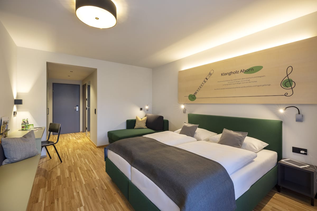 Een moderne hotelkamer met een groot bed, een bureau en een stoel. Er hangt een kunstwerk aan de muur en op een kleine tafel staat een lamp.