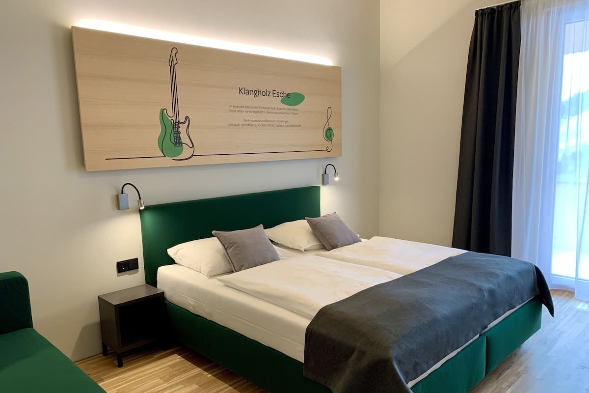 Een hotelkamer met een groot bed, een groen hoofdeinde en een kunstwerk aan de muur met een gitaar.