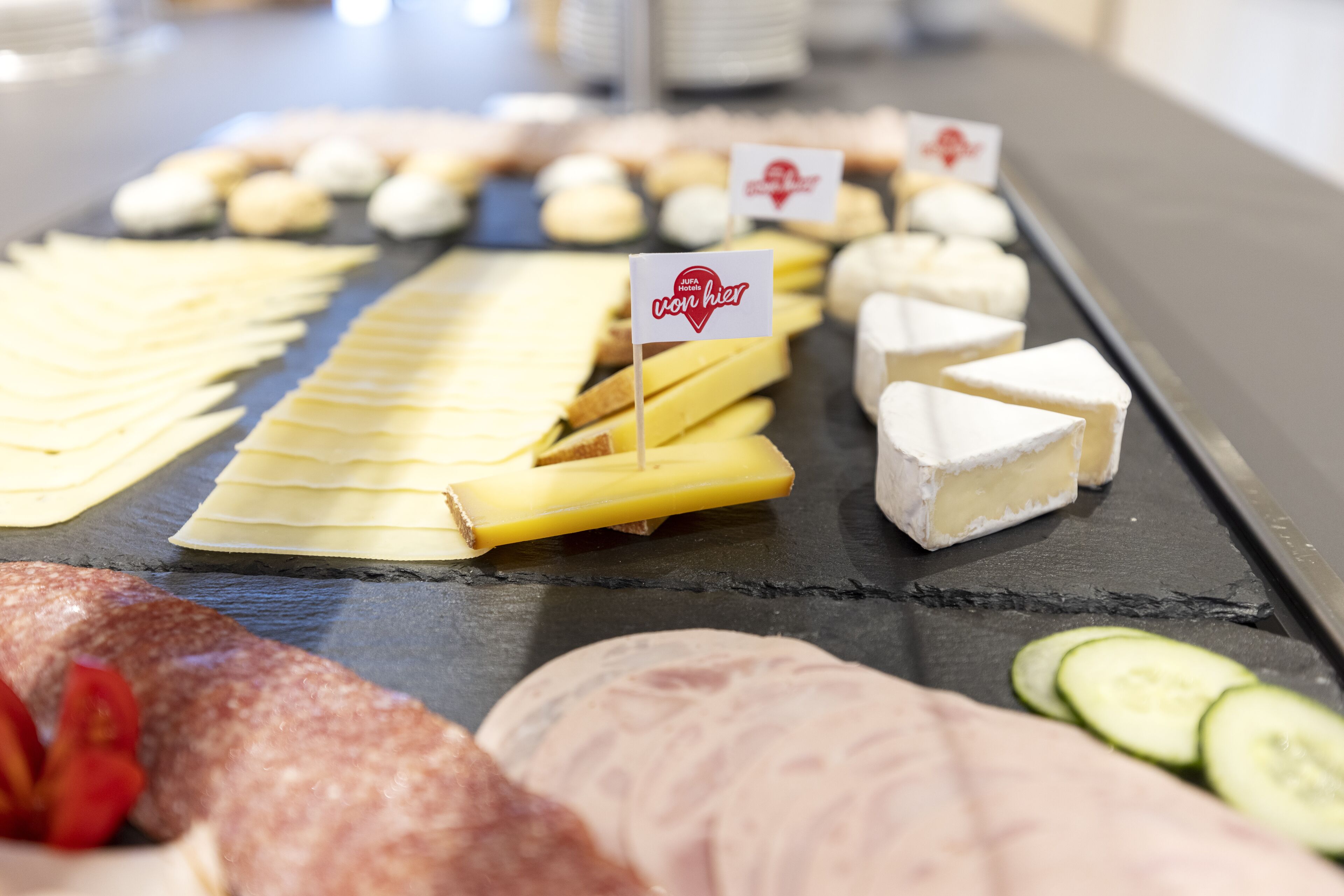 A cheese board with various types of cheese and sliced cucumbers.