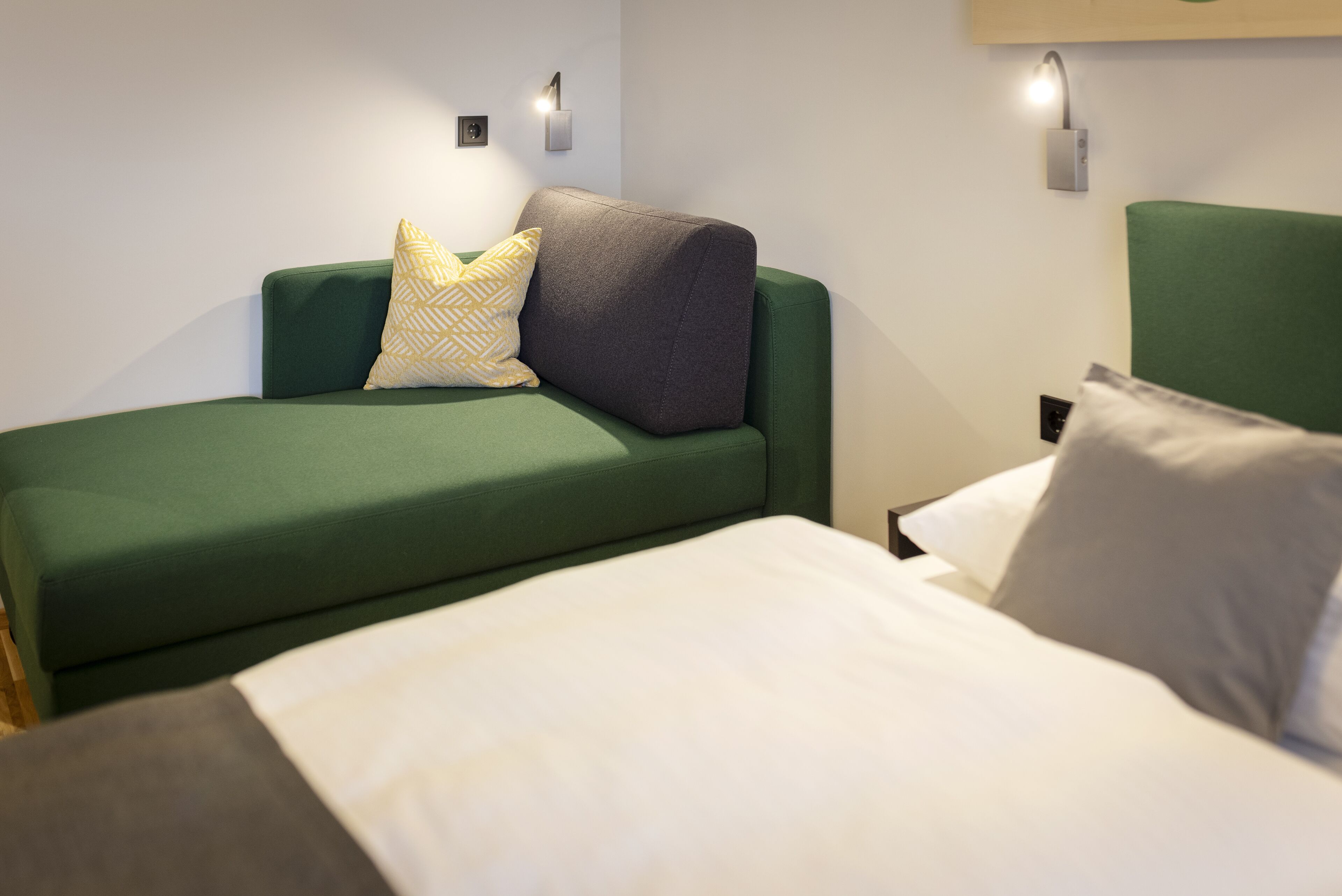 Une pièce avec un canapé vert, un lit blanc et deux appliques murales.