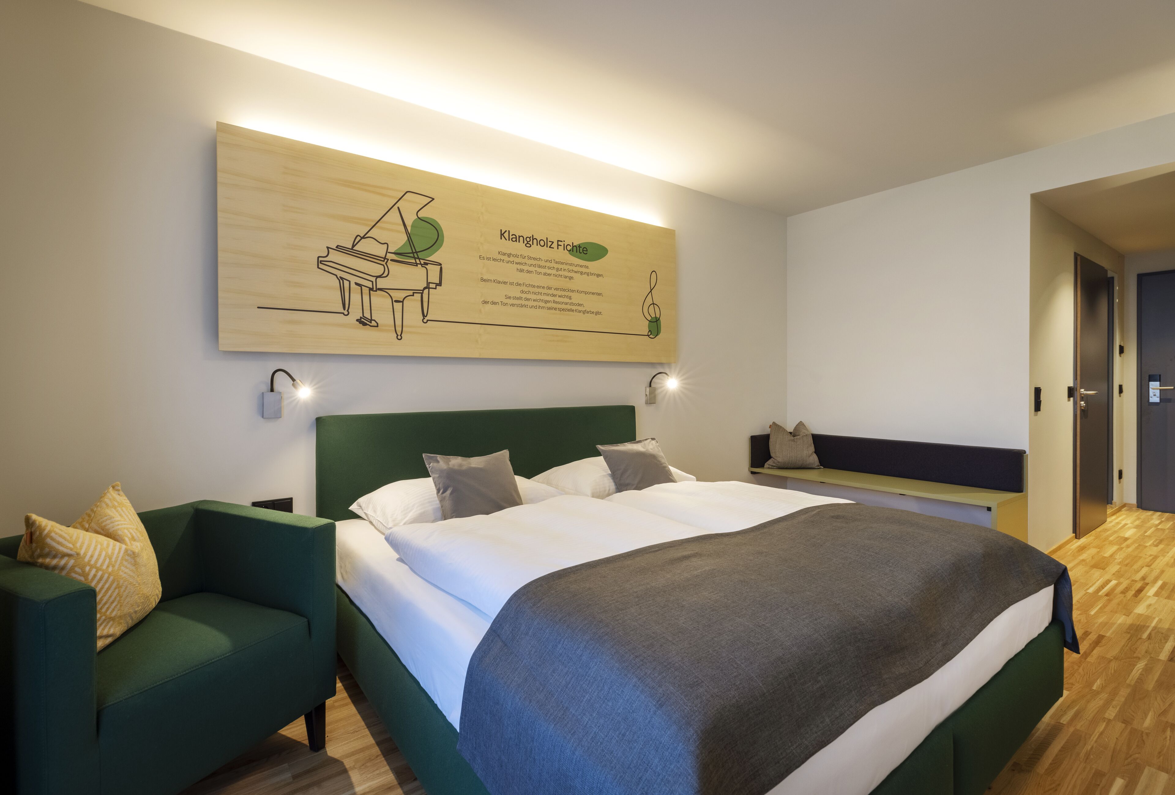 A hotel room with a large bed, a green sofa, and a wall-mounted artwork of a piano.