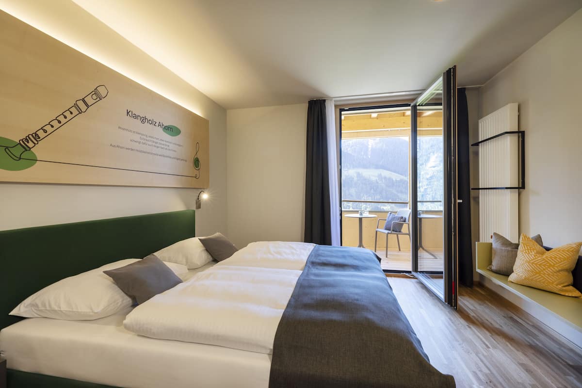 Een hotelkamer met een bed, uitzicht op bergen, een balkon en een informatietafel aan de muur.