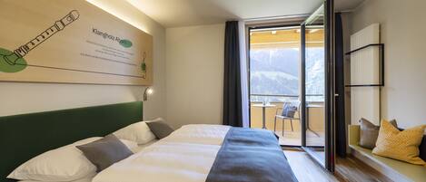 Ein Hotelzimmer mit Bett, Blick auf Berge, einem Balkon und einer Wandtafel mit Informationen.