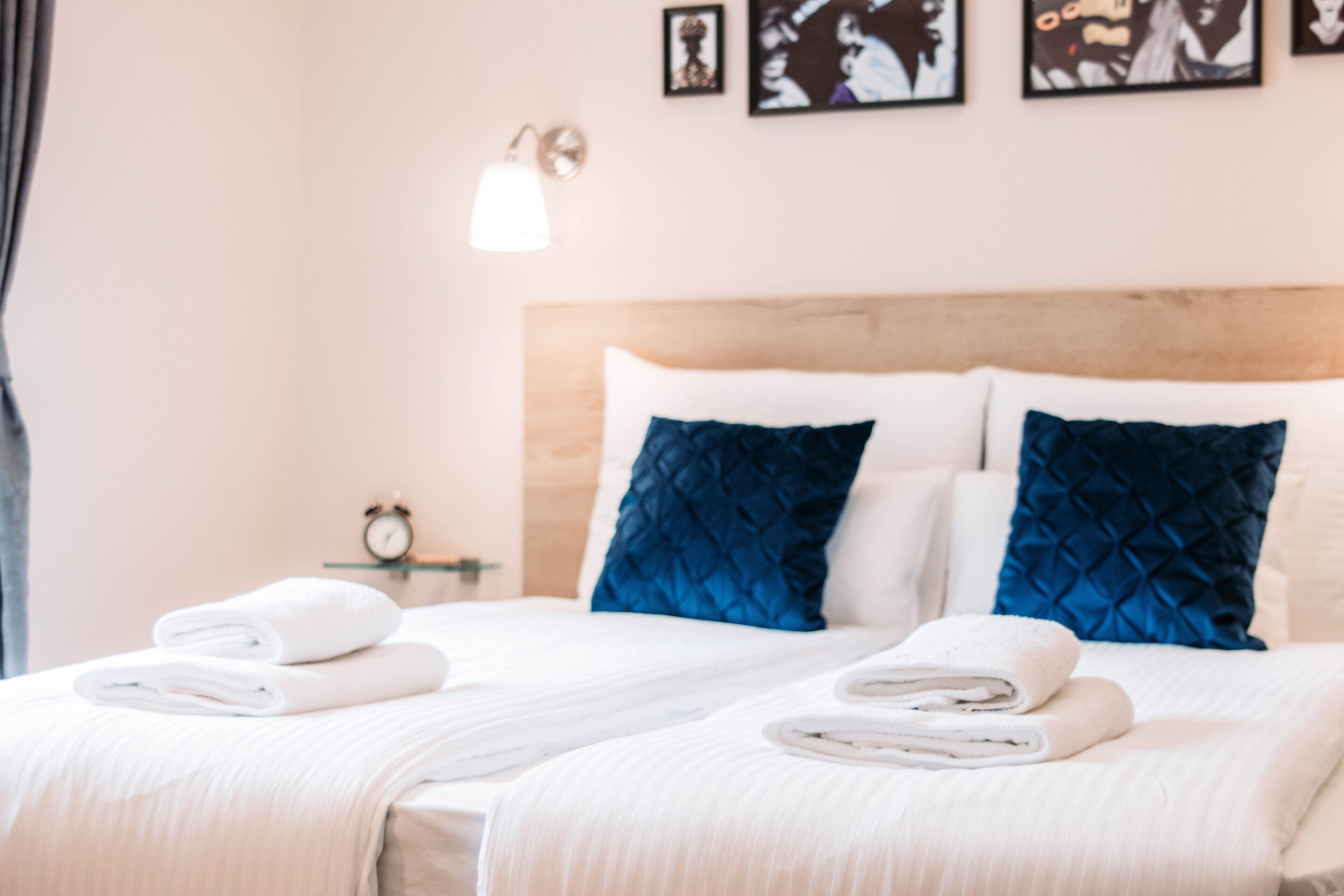 A hotel room with a bed, two pillows, a bedside table with a lamp, and a wall clock.