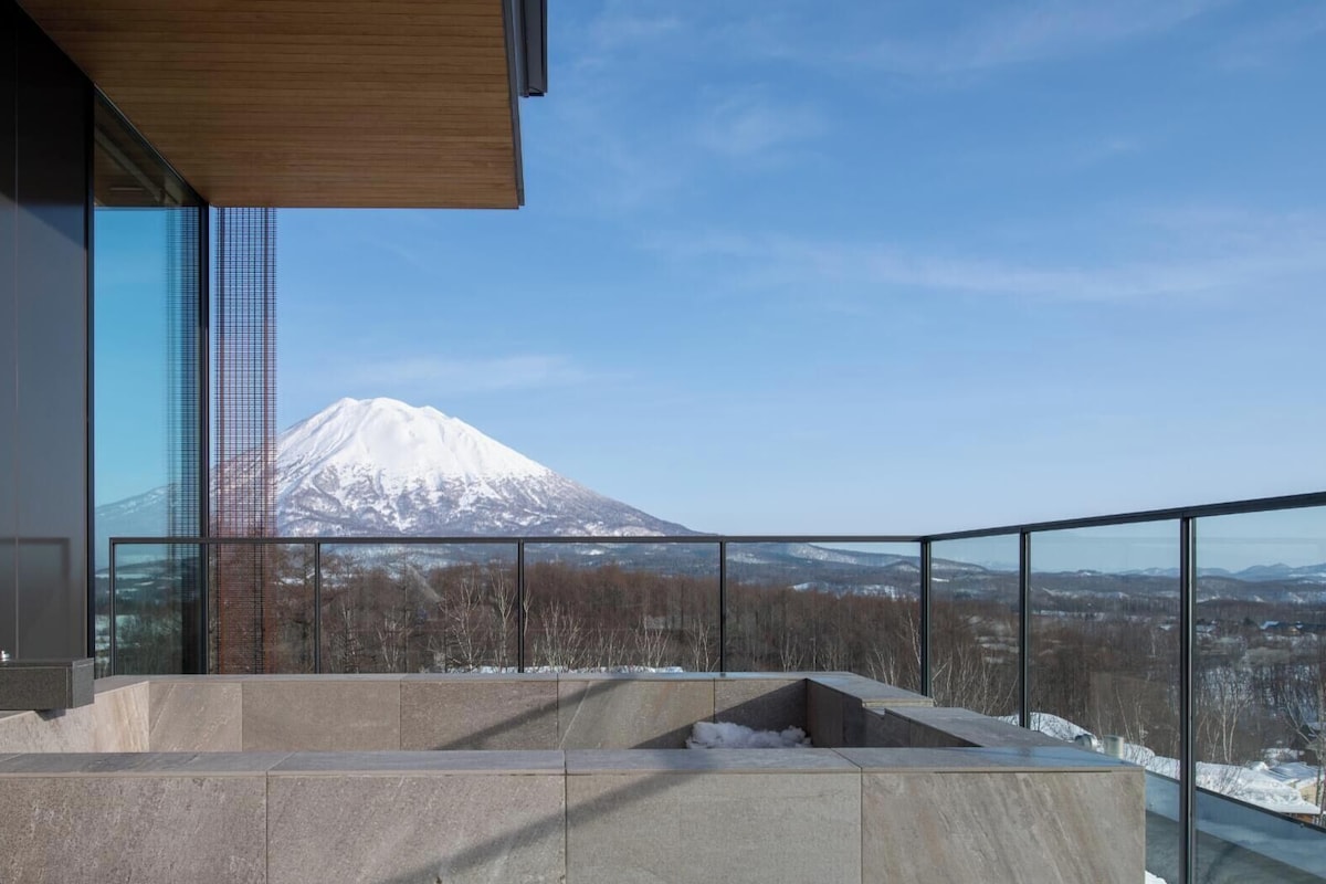 Un bâtiment moderne doté d’une grande baie vitrée et offrant une vue sur une montagne enneigée.