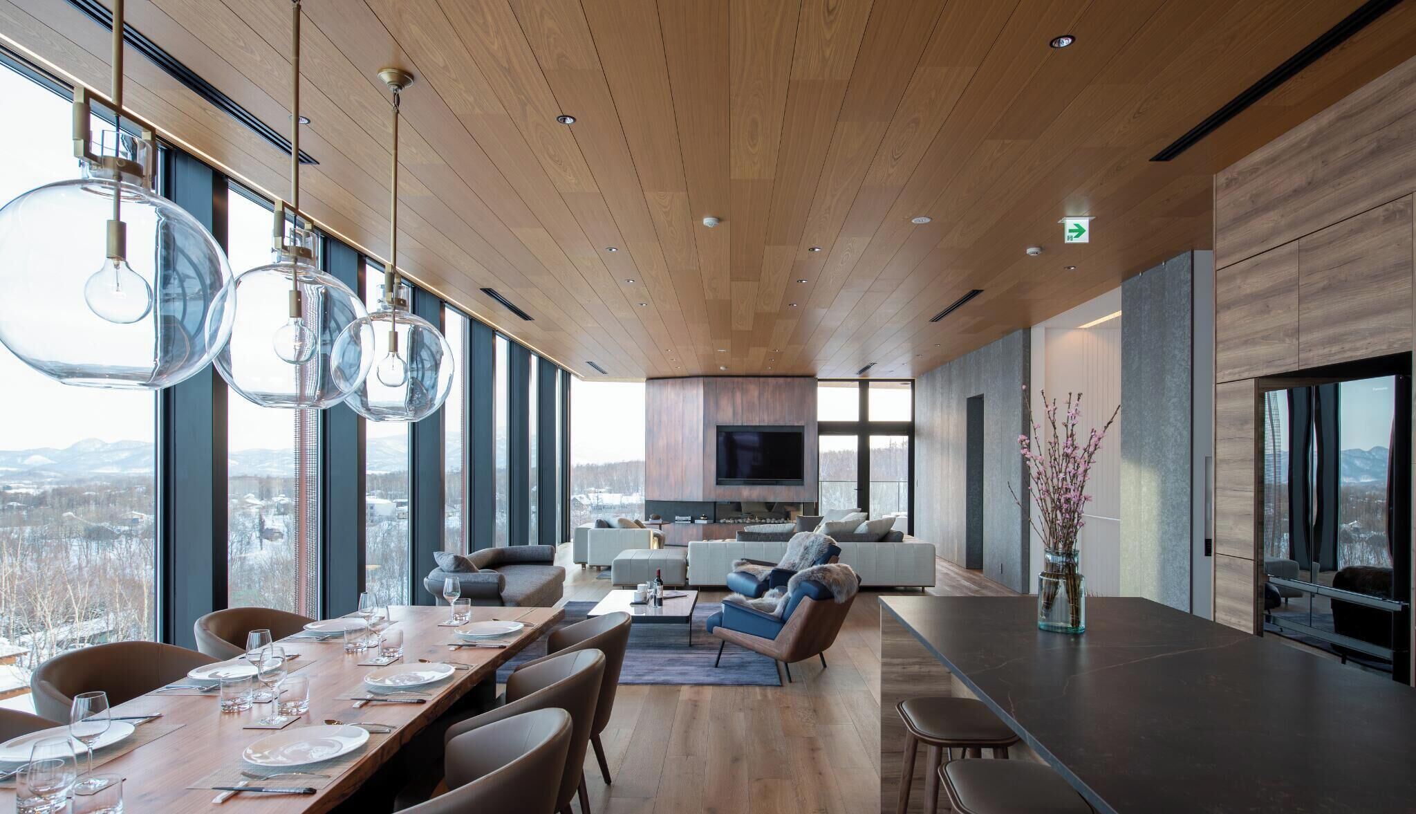 A modern interior with a dining area, sofas, a kitchen, and large windows offering a view.