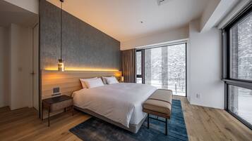 A modern bedroom with a large bed, bedside tables, a bench, a view of snowy trees through large windows, and a textured wall.