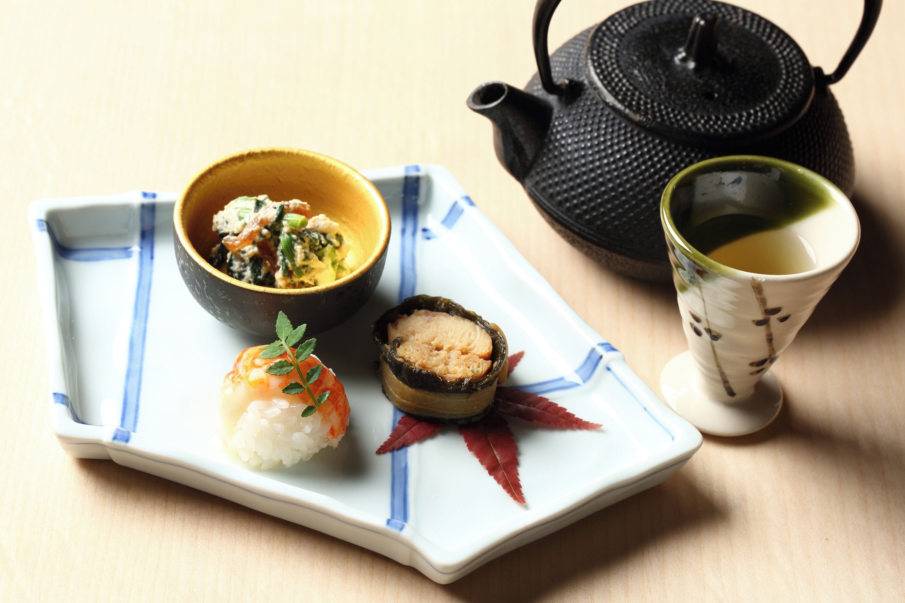 A tray with sushi, a bowl of soup, and a teapot.