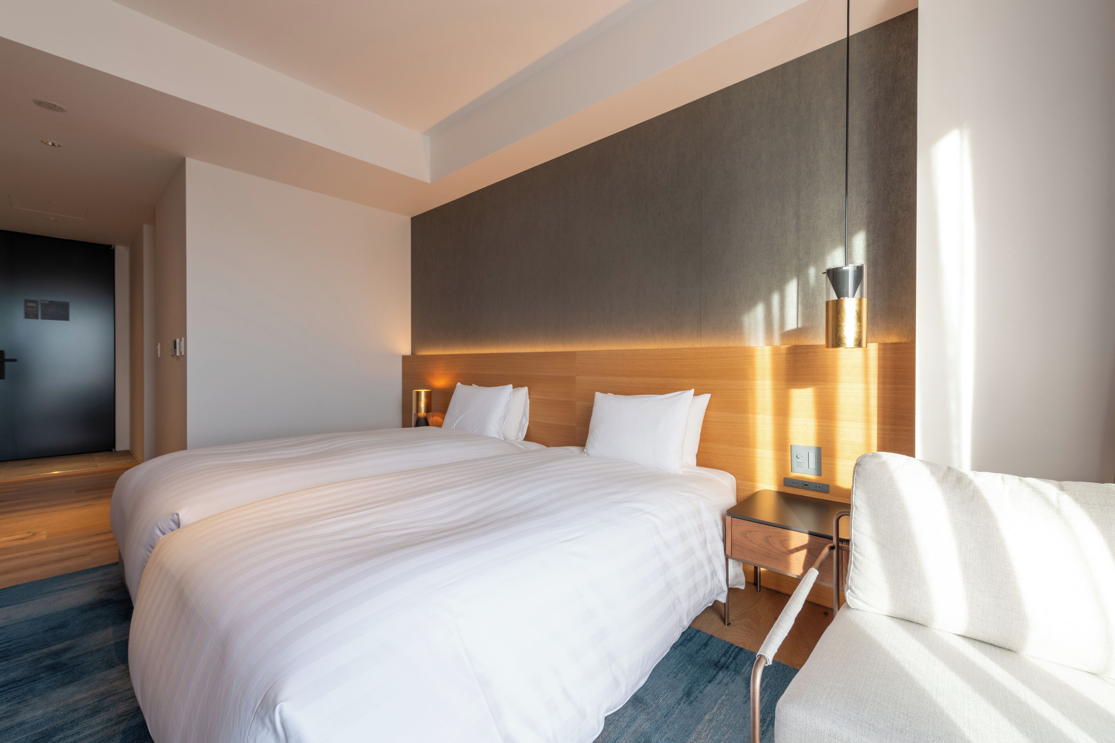Habitación de hotel moderna con una cama grande, un sofá, una mesita de noche y una lámpara de pared.