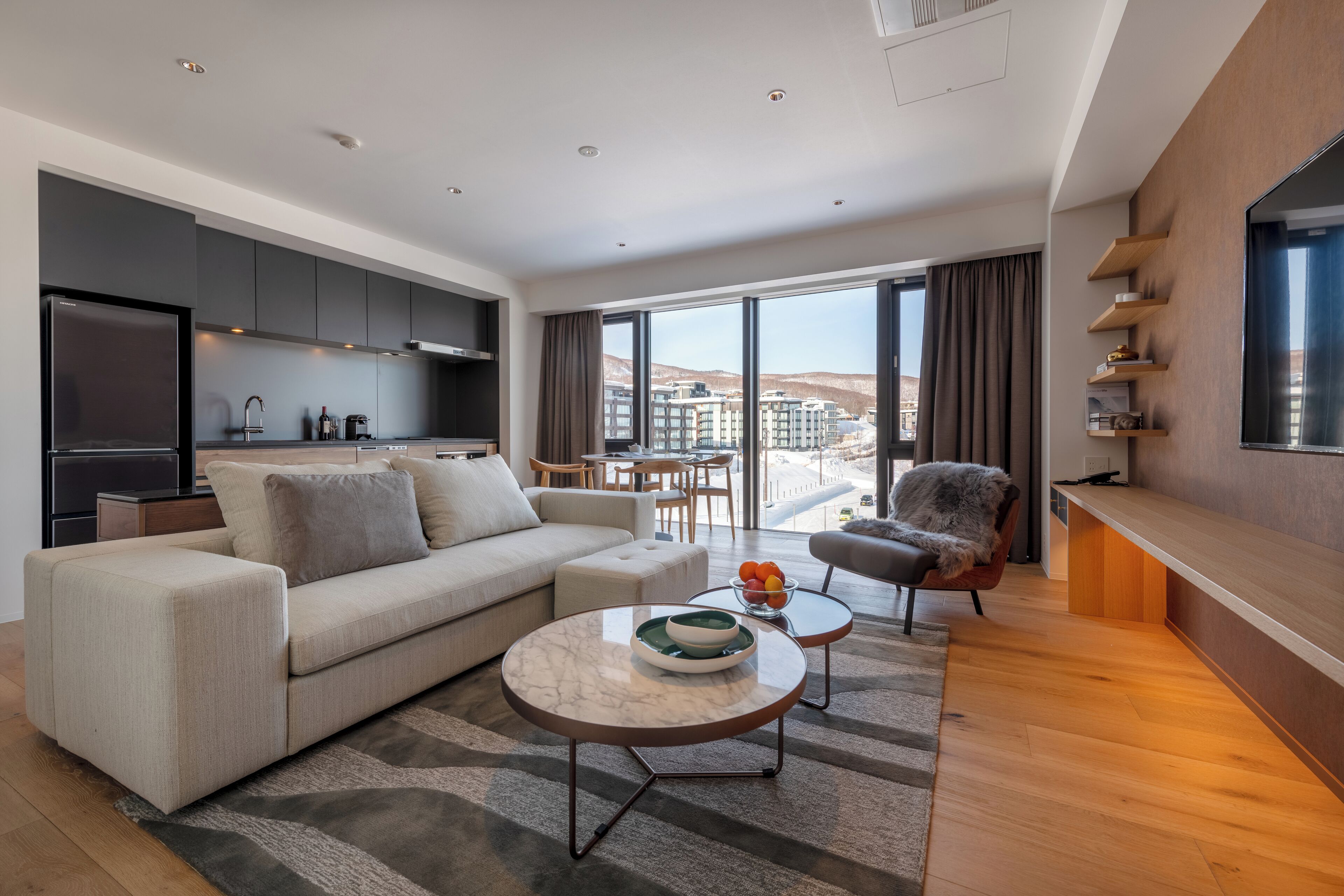 A modern living room with a sofa, coffee table, and a view of a cityscape through large windows.