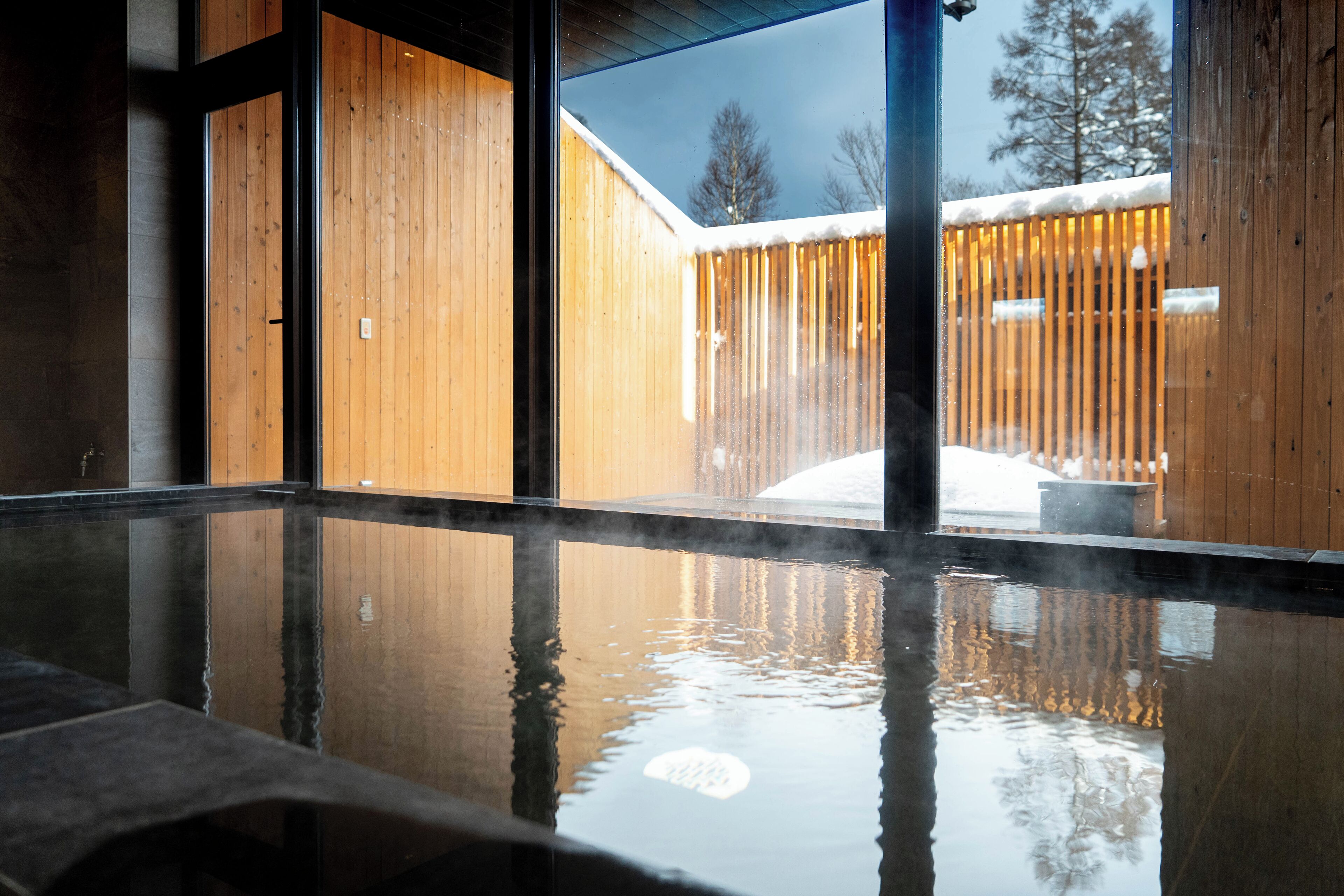 A hot spring area with a wooden deck and snow-covered fence visible through the glass.