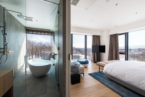 Une chambre d’hôtel moderne avec un grand lit, une baignoire, un canapé et une télévision.