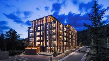 A modern multi-story hotel with a glass facade, located in a wooded area.