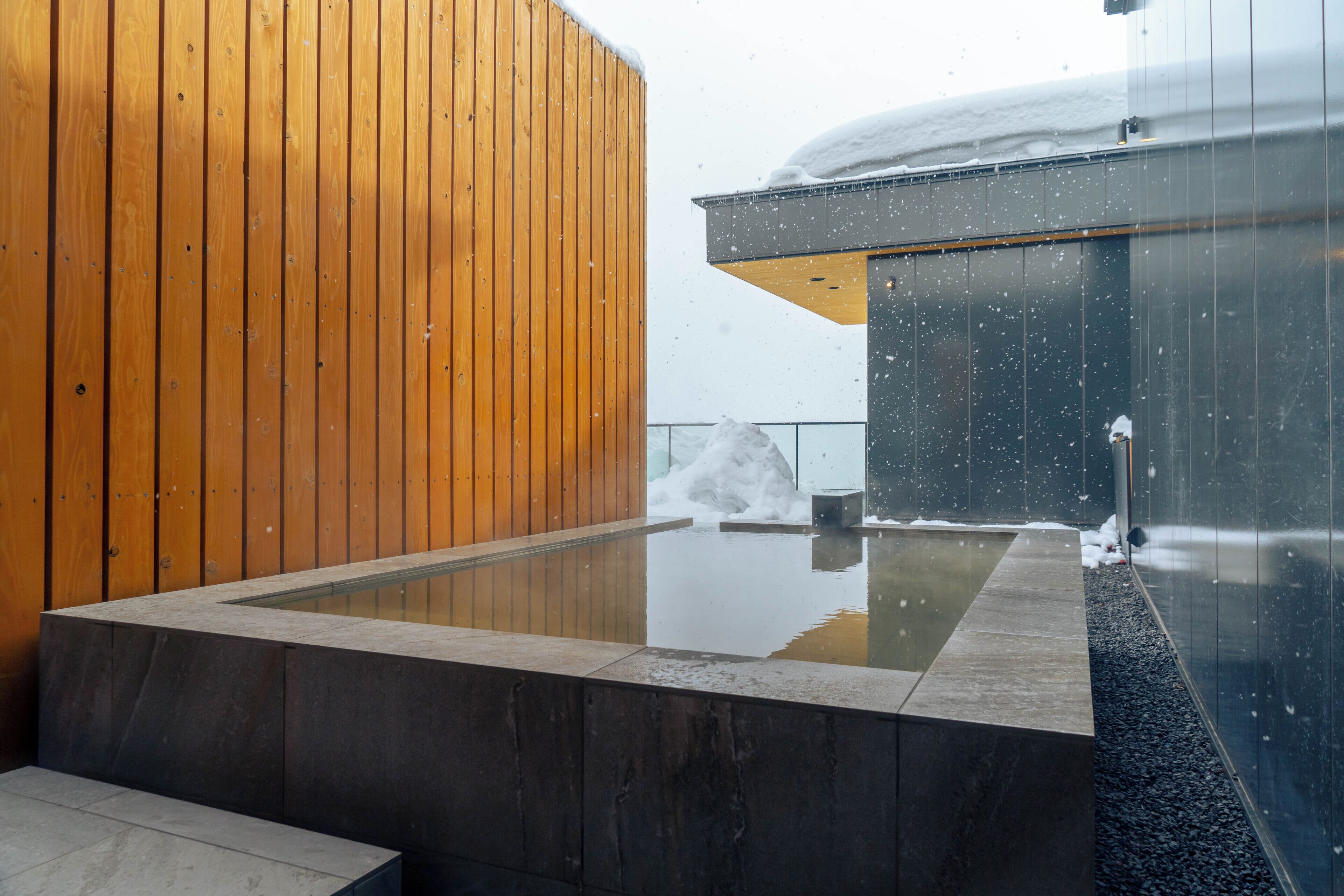 Une piscine intérieure moderne aux murs en bois et en verre, entourée de neige.