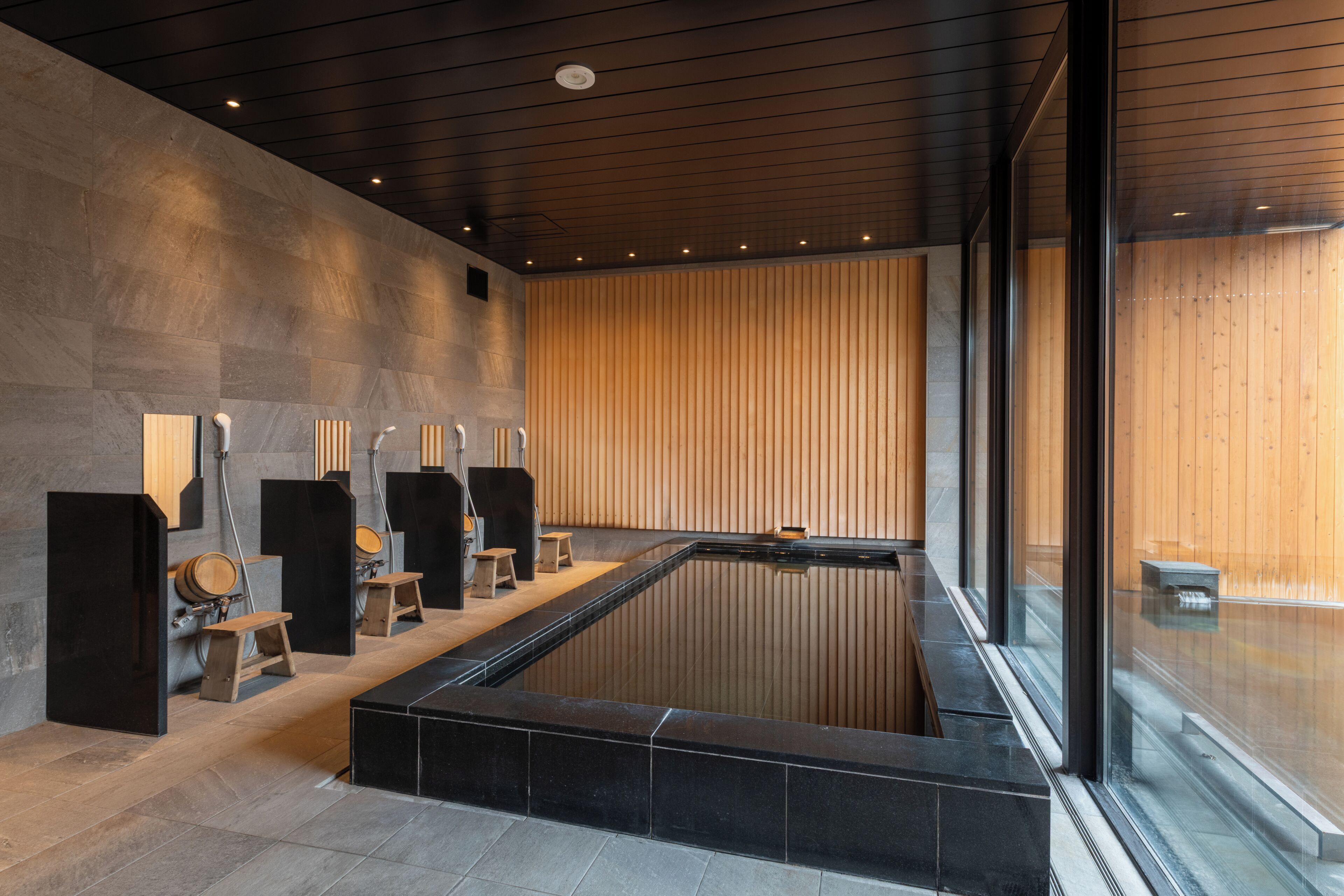 A modern spa area with a large rectangular pool, wooden benches, and a stone wall.