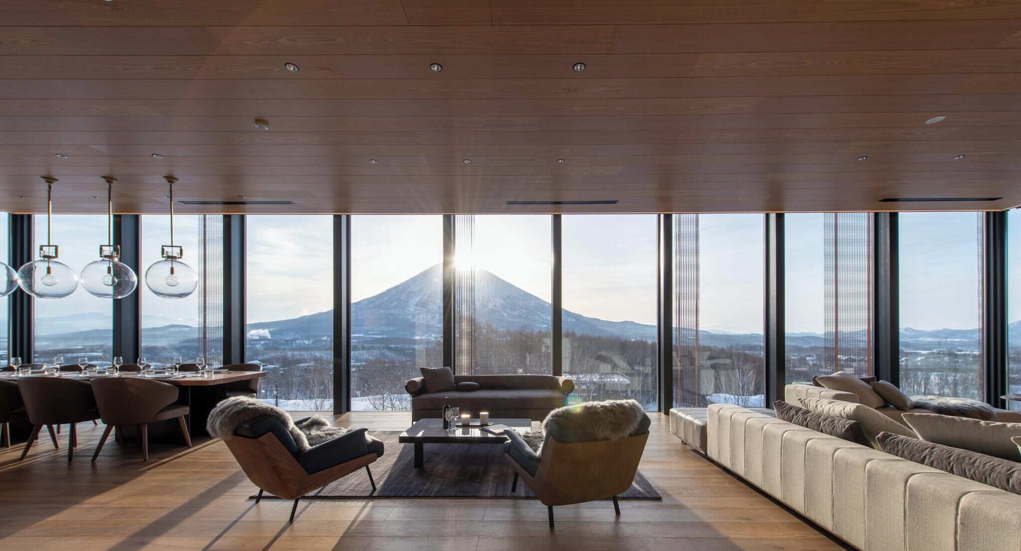 A modern living room with a large window, a sofa, a coffee table, and a dining area.
