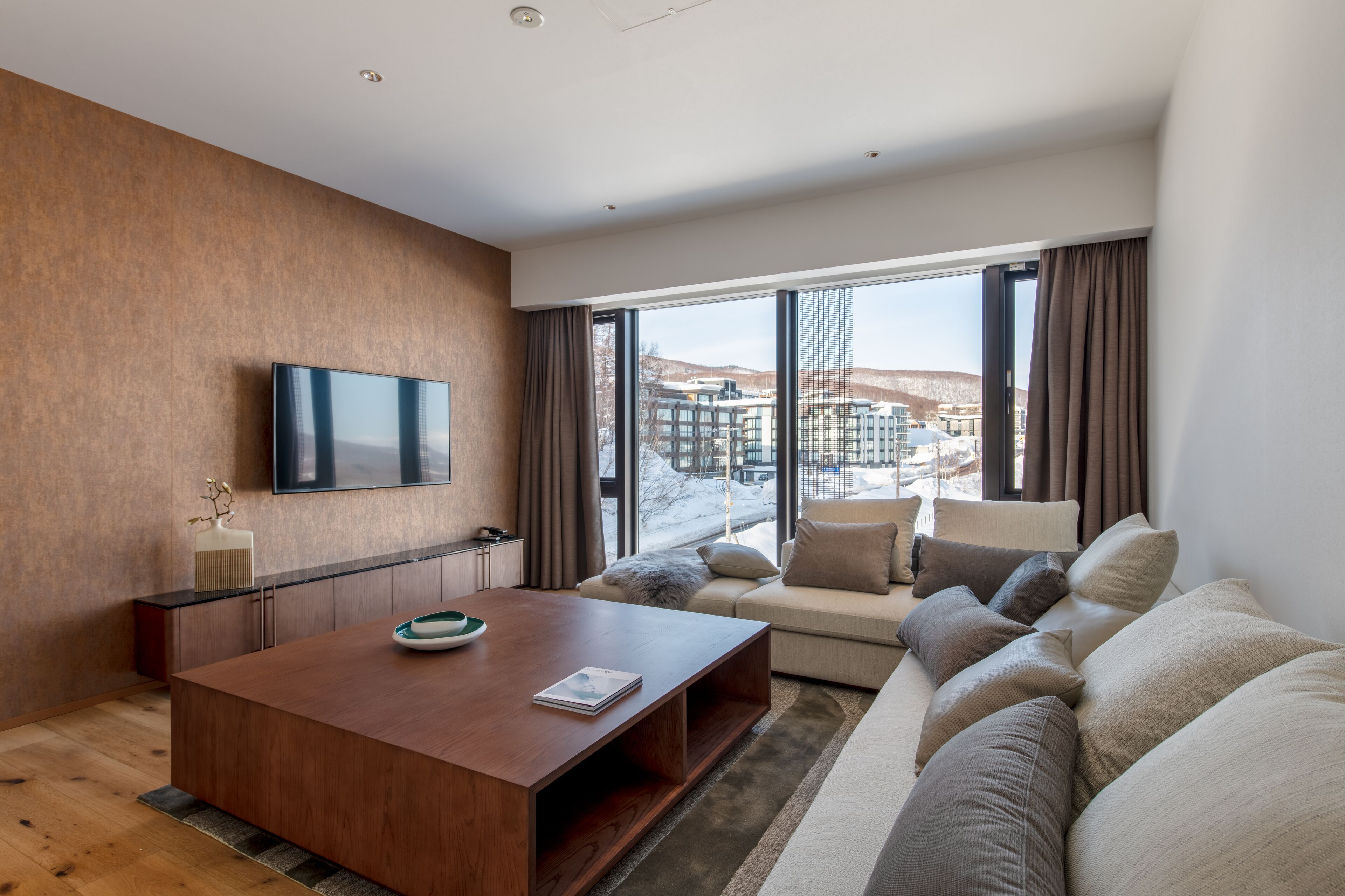 A modern living room with a wooden coffee table, a sofa, and a TV mounted on the wall.