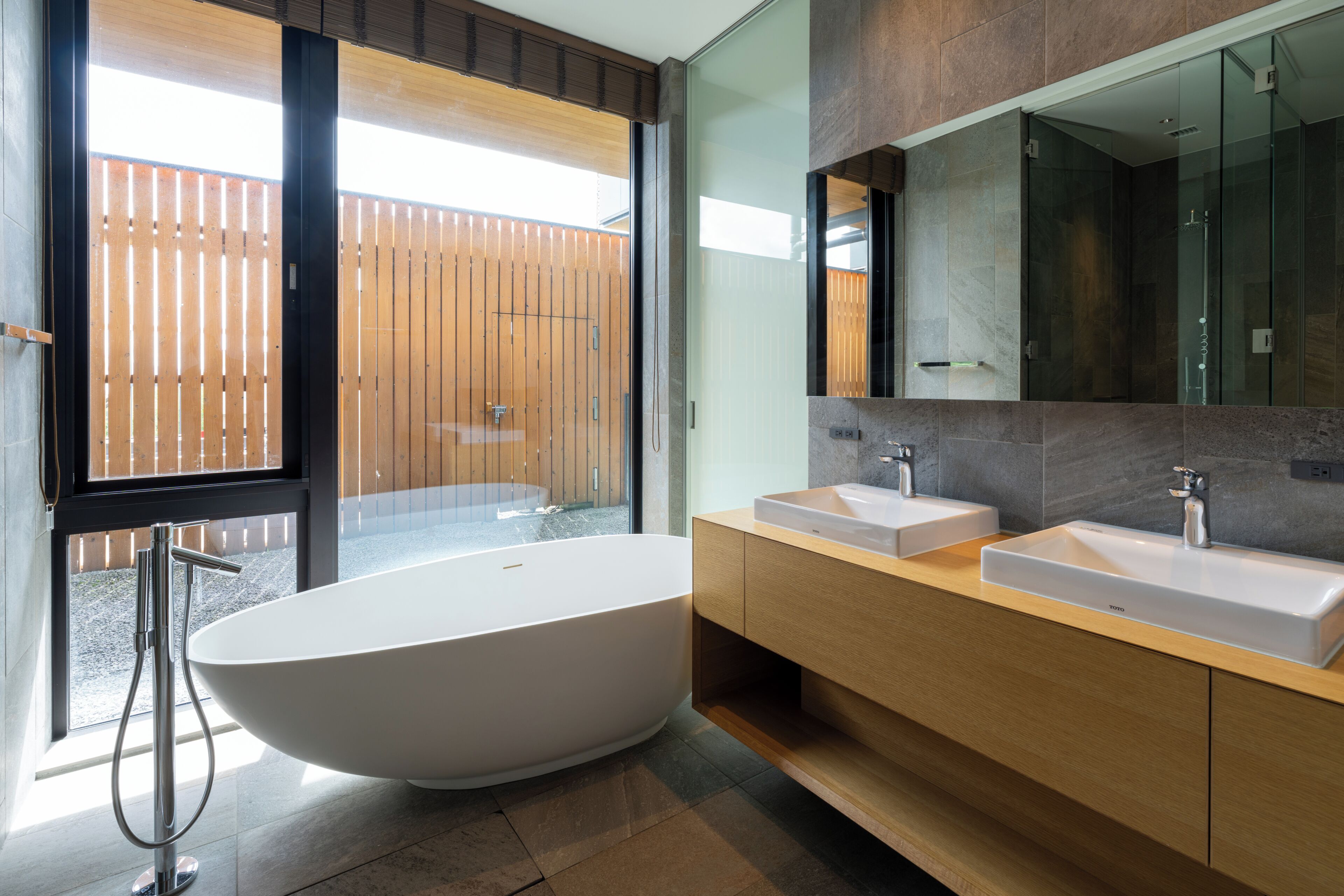 A modern bathroom with a freestanding bathtub, two sinks, and a large mirror.