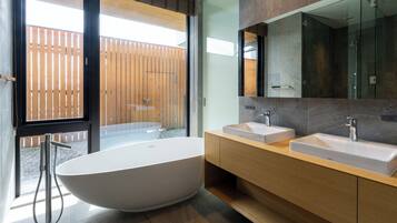 A modern bathroom with a freestanding bathtub, two sinks, and a large mirror.