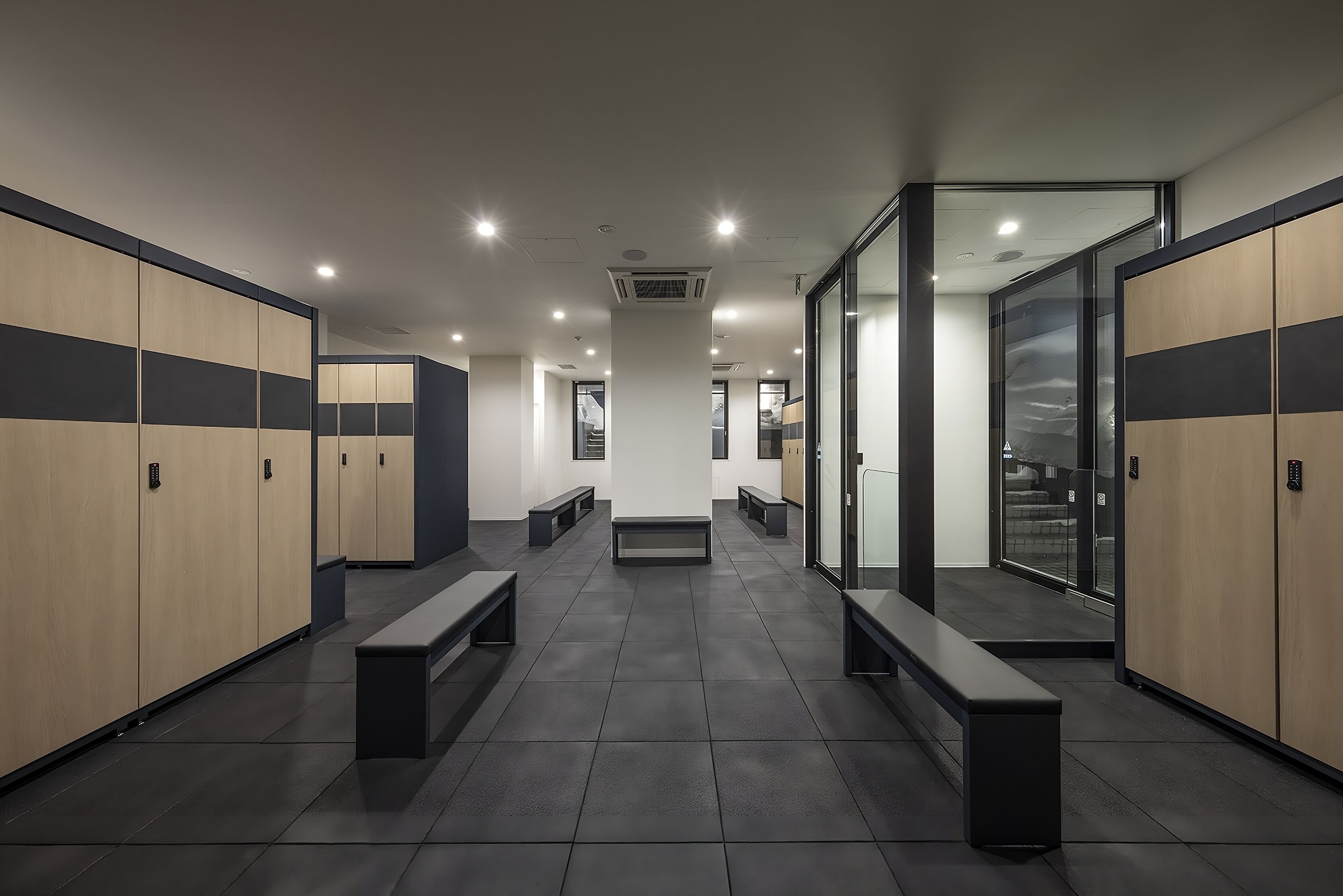 A modern locker room with benches, lockers, and a glass partition.