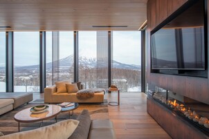 Un salon moderne doté d’un grand téléviseur, d’une cheminée et d’un canapé placé face à une grande fenêtre offrant une vue sur les montagnes.