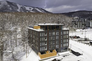 Un edificio moderno de varios pisos, rodeado de árboles nevados y montañas al fondo.